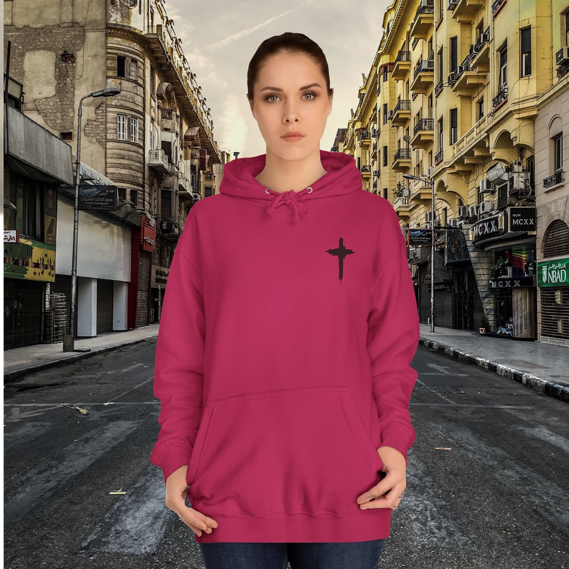 Woman wearing a pink hoodie with a black cross design on a city street background